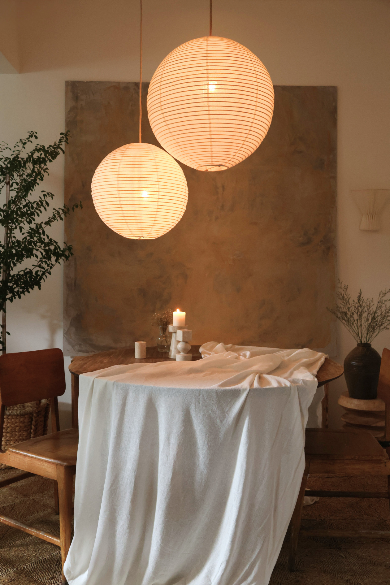 Two spherical pendant lights hanging above a dining table with a white tablecloth, candle, and decorative items.